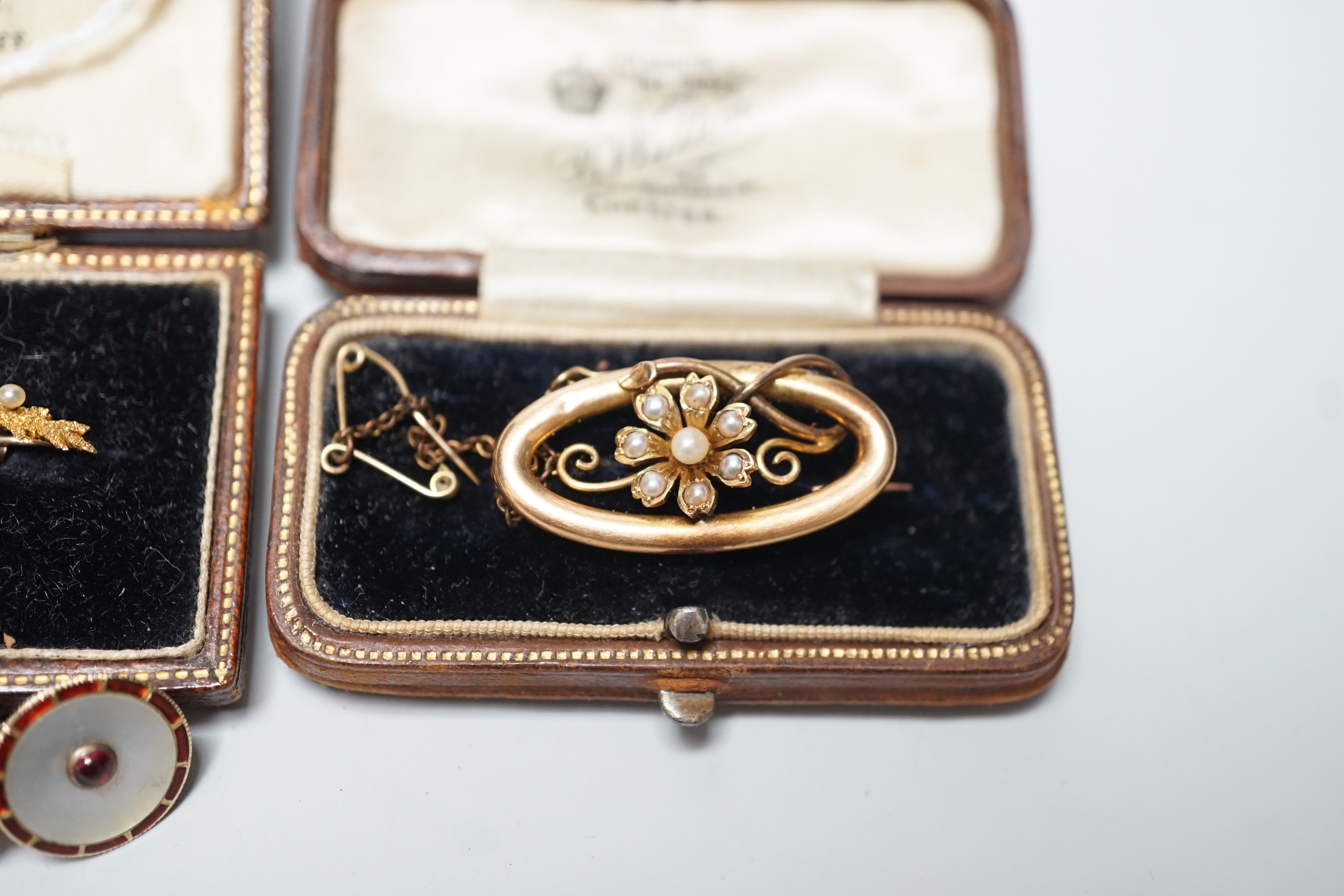 An early 20th century 15ct and seed pearl set leaf brooch, 51mm, one other 15ct and seed pearl brooch and a pair of 15ct, enamelled and gem set ear studs (converted buttons), gross weight 10 grams.